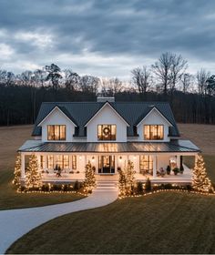 a large white house with christmas lights on the front porch and trees in the yard