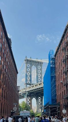 people are walking on the sidewalk in front of some tall buildings and a large bridge