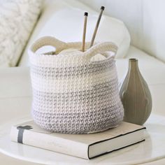 a crocheted basket sitting on top of a white table next to a book