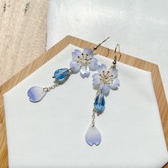 These earrings are a beautiful and unique accessory that would make a perfect gift for a special woman in your life. They are handmade and feature cherry blossom petals in shades of blue and white, made from shrink plastic material. The petals are intricately designed to resemble the delicate and graceful sakura flowers that are popular in Japanese culture. Adding to the beauty of these earrings are crystal drops that dangle from the petals, giving them an elegant and sophisticated look. The cry Handmade Flower Crystal Earrings For Gifts, Elegant Light Blue Dangle Flower Earrings, Elegant Light Blue Flower Earrings, Light Blue Flower Shaped Earrings For Gift, Handmade Light Blue Drop Flower Earrings, Light Blue Crystal Drop Earrings For Gift, Light Blue Crystal Earrings For Gift, Blue Flower-shaped Party Earrings, Blue Flower-shaped Earrings For Gifts