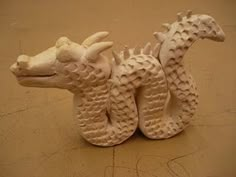 a white dragon figurine sitting on top of a brown floor next to a wall