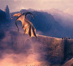 a dragon flying over a bridge in the middle of a foggy mountain area with people standing on it