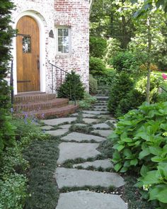 a brick house with steps leading to the front door and green plants in the foreground