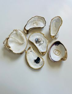 five pieces of jewelry sitting on top of a white table next to an open oyster shell