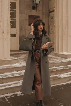 a woman is standing outside in the snow with her hand on her head and holding a purse