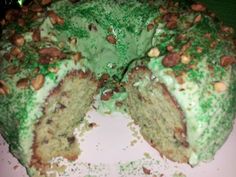 there is a cake with green frosting and nuts on the top, cut in half