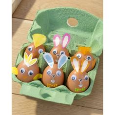 four decorated eggs in an egg carton on a wooden floor with the faces of rabbits painted on them