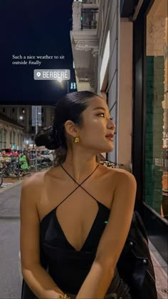 a woman in a black dress sitting on the side of a street next to a building