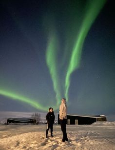 two people are standing in the snow under an aurora borel light, with one person looking at the camera