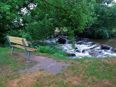 a park bench sitting on top of a grass covered field next to a river filled with water