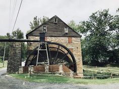 an old brick building with a water wheel in front of it on the side of a road