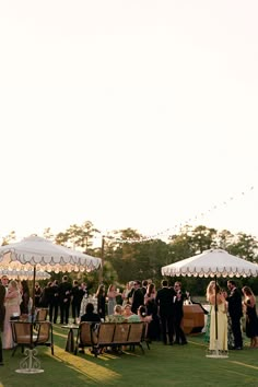 a group of people standing around tables with umbrellas over them at a formal event