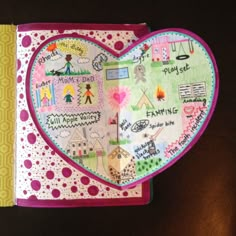 a heart shaped book with writing on the pages and pictures in the middle, sitting on top of a table