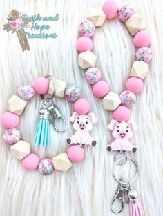 a pink and white bracelet with two charms on top of it next to a keychain