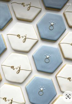 wedding rings are on top of some blue and white hexagonal cookies with gold lettering