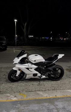 a white and black motorcycle parked in a parking lot at night with its lights on