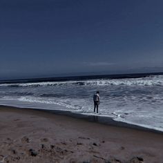 a man standing on top of a sandy beach next to the ocean