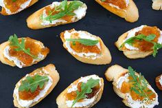 small appetizers are arranged on a black surface with green garnishes