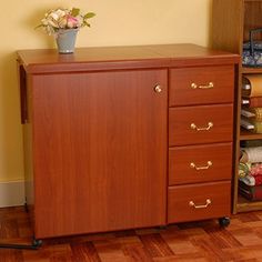 a wooden cabinet with three drawers and a vase on top of it, in front of a yellow wall