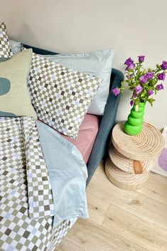 a bed covered in lots of pillows next to a green vase with flowers on it