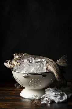 a fish is sitting in a colander with ice cubes on the table next to it