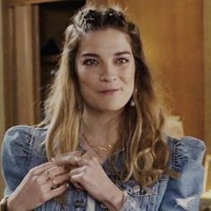 a woman with long hair wearing a denim shirt and gold bracelets is looking at the camera