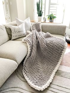 a couch with a blanket on top of it next to pillows and a potted plant