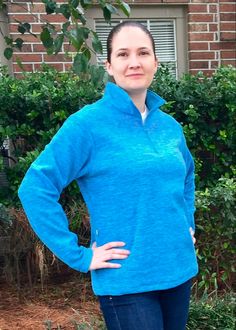 a woman standing in front of a brick building with her hands on her hips, wearing a blue jacket and jeans