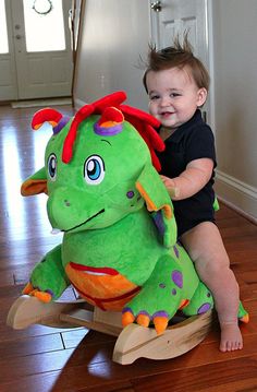 a toddler sitting on a rocking toy with a green dragon stuffed animal in it's arms