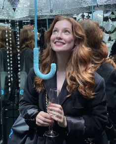 a woman standing under an umbrella holding a glass in her hand and smiling at the camera