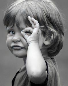 a black and white photo of a little boy holding his hand up to his face