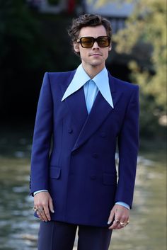 a man in a blue suit and sunglasses standing next to a boat on the water