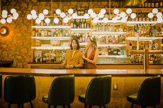 two women sitting at a bar with bottles behind them