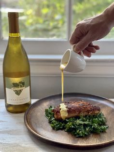 a person pours dressing on top of a plate next to a bottle of wine