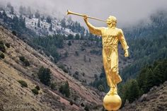 a golden statue with a trombone in its hand on top of a rock near mountains