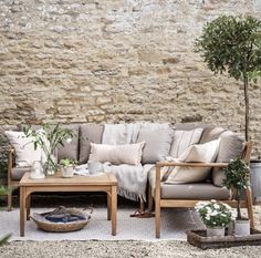 a couch and table in front of a stone wall with potted plants on it