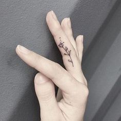 a woman's hand with a small flower tattoo on it, holding up her fingers