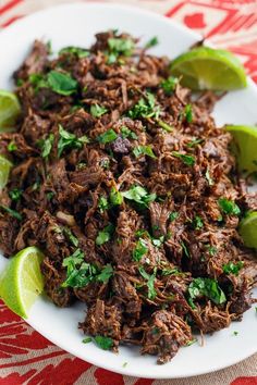 shredded beef with limes and cilantro on a white plate, ready to be eaten