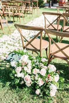 an arrangement of flowers on the ground in front of wooden chairs at a wedding ceremony