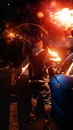 a man standing next to a blue car in front of a bunch of fireballs