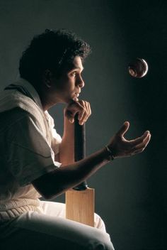 a man sitting in a chair holding a baseball bat and ball with his right hand