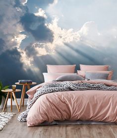 a bed with pink sheets and pillows in front of a cloudy sky wallpaper mural