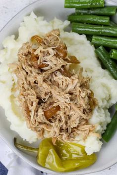 a white plate topped with mashed potatoes covered in meat and veggies next to green beans