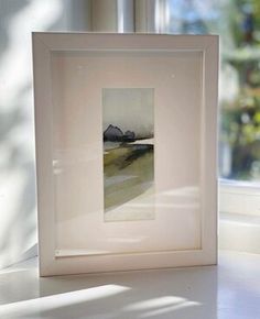 a painting in a white frame sitting on a window sill