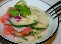 a white plate topped with cucumber and tomato salad next to a knife and fork