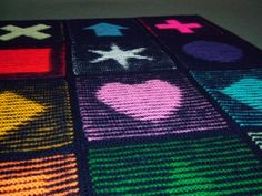 four knitted squares with hearts and crosses on them, all in different shades of rainbow