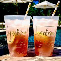 two glasses filled with drinks sitting on top of a wooden table next to a pool