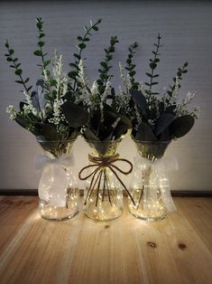 two vases with flowers and greenery are sitting on a table