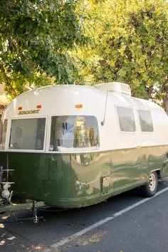 a green and white trailer parked on the side of a road next to a tree