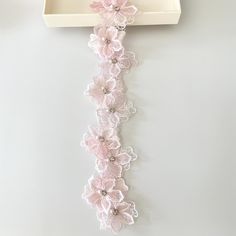 a cross with pink flowers hanging from it's side on a white wall next to a box